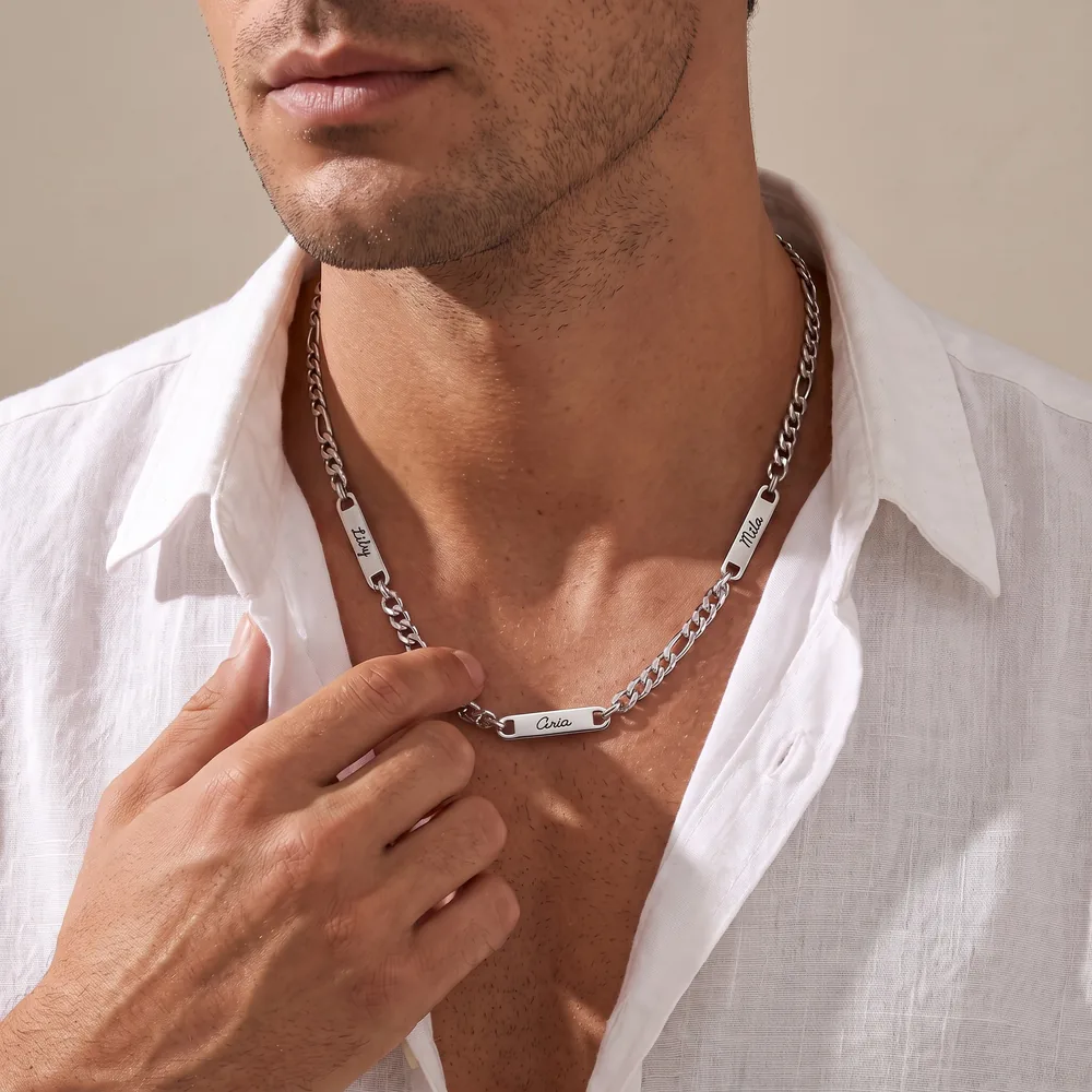Man in a white linen shirt wearing a silver figaro-chain necklace with three engraved name bars