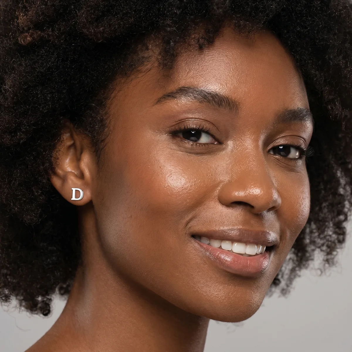 Smiling woman with curly hair wearing a silver letter D stud earring