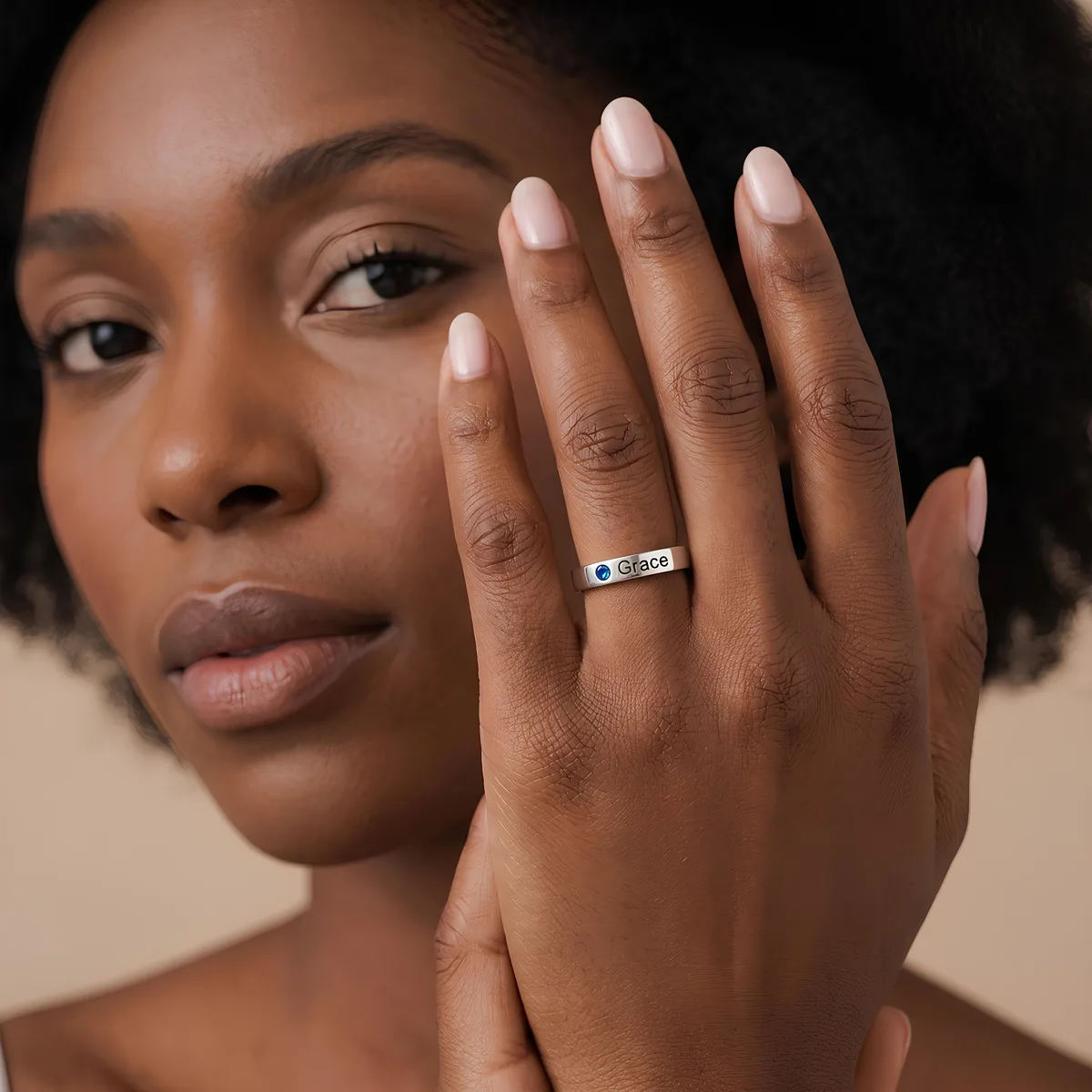 Woman holding her hand to her face, showing a silver ring engraved with the name Grace and a blue birthstone